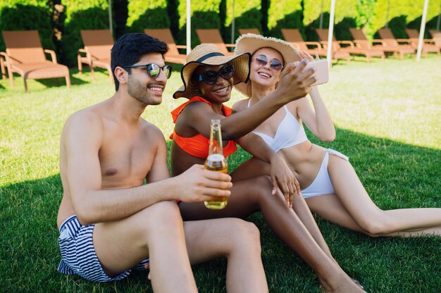 Des amis joyeux boivent ensemble de la bière près de la piscine. Des gens heureux s'amusant pendant les vacances d'été, une fête de vacances au bord de la piscine en plein air pour bronzer