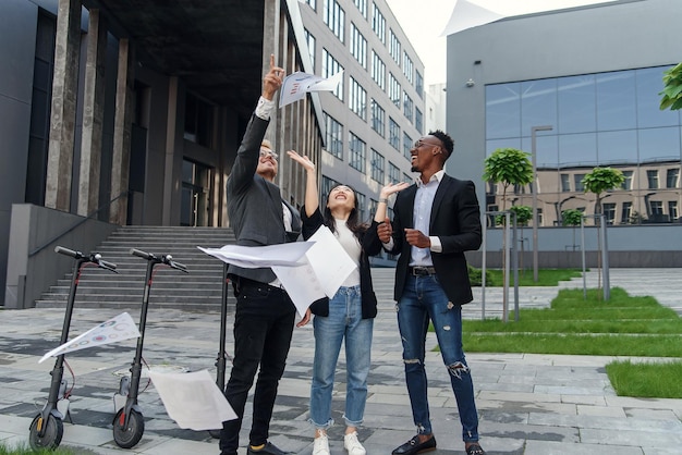 Photo des amis joyeux de différentes races s'amusent ensemble près du bureau et éparpillent des papiers d'affaires.