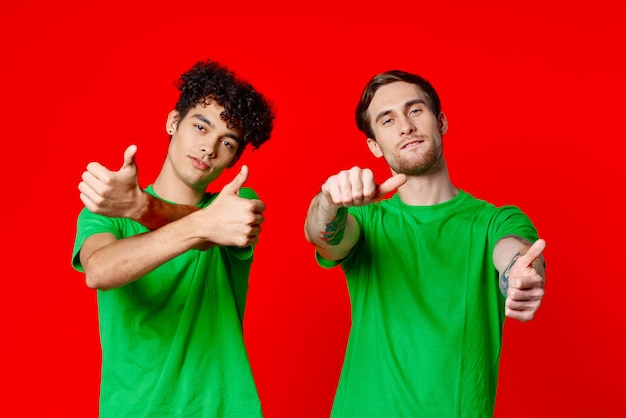 Amis joyeux en t-shirts verts gesticulant avec les mains émotions fond rouge