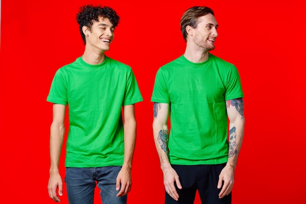 Des amis joyeux en t-shirts verts se tiennent à côté d'un fond rouge