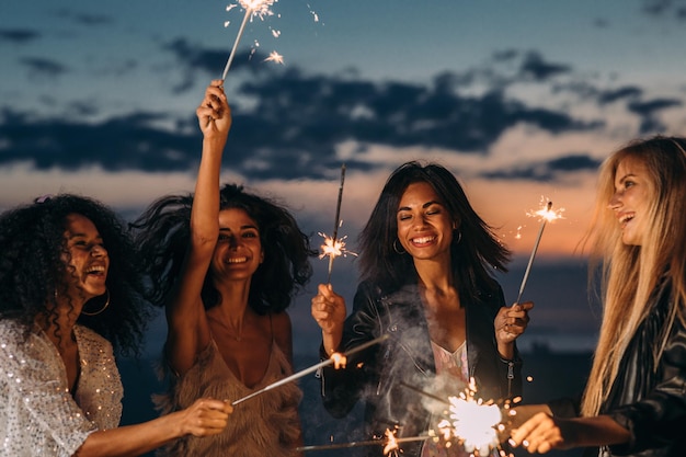 Des amis joyeux tenant des étincelles tout en se tenant contre le ciel