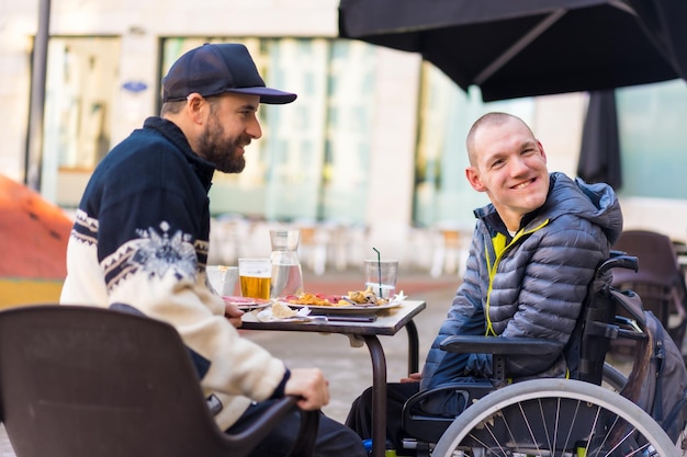 Amis mangeant dans un fauteuil roulant de personne handicapée de terrasse de restaurant