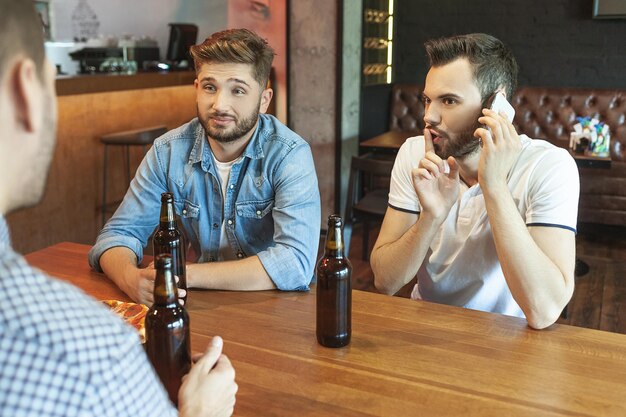 Amis masculins buvant de la bière avec de la pizza ensemble un homme parlant sur smartphone