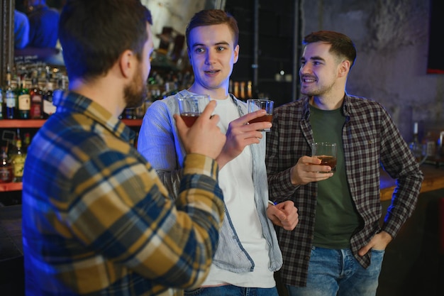 Amis masculins passant du temps ensemble au bar et s'amusant Hommes barbus souriants se regardant et communiquant Hommes tenant des verres en cristal de whisky ou de scotch