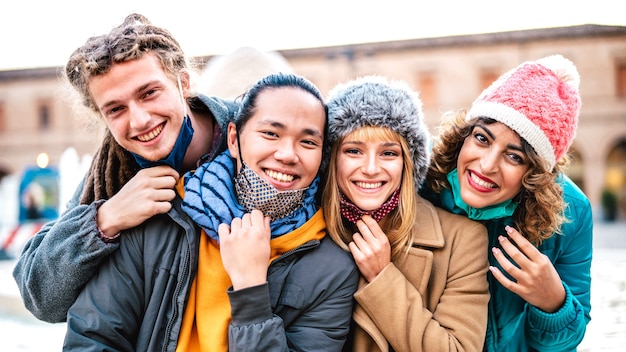 Amis multiculturels prenant selfie heureux portant un masque et des vêtements d'hiver