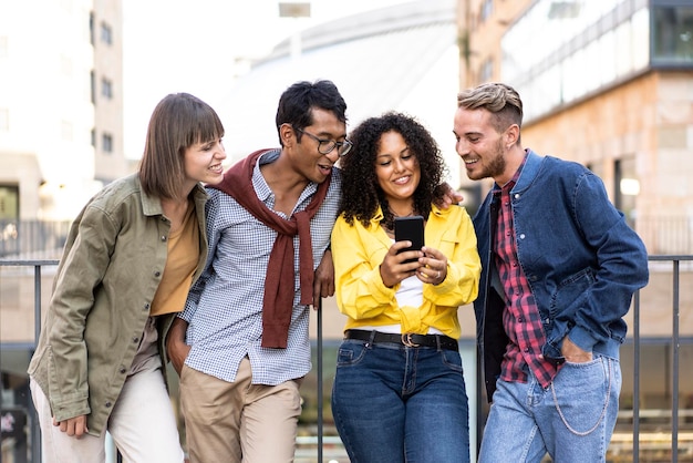 Amis multiculturels s'amusant avec un téléphone portable dans la cour du collège du campus Jeunes hommes et femmes passant du temps ensemble à partager une vidéo amusante sur un smartphone Focus sur une fille bouclée colombienne