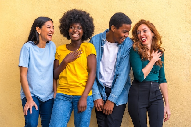 Amis multiethniques contre le mur jaune s'amusant souriant communauté internationale de jeunes