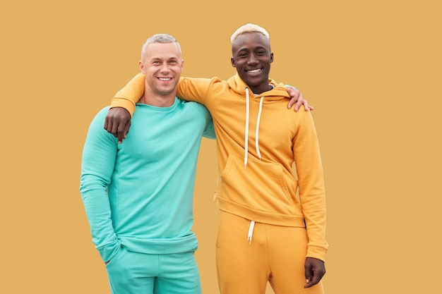 Amis multiethniques. Deux hommes de couleur différente d'ethnie afro-américaine noire et d'ethnie caucasienne blanche debout sur fond jaune isolé. Vêtements de sport actifs habillés. amitié interraciale