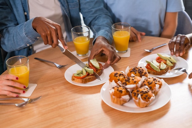 Amis multiethniques lors d'un petit-déjeuner avec du jus d'orange et des muffins à la maison coupant les toasts