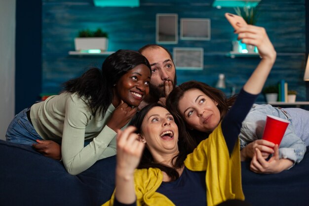 Amis multiethniques souriant à la caméra tout en souriant femme prenant selfie