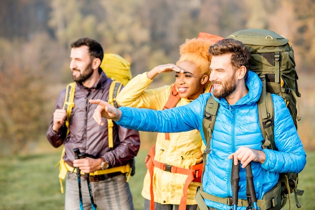 Amis multiethniques en vestes colorées randonnée avec sacs à dos dans la forêt
