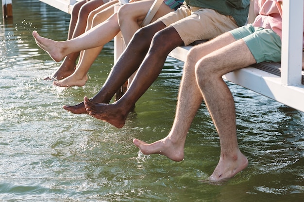 Amis multiraciaux aux pieds nus en tenue décontractée aux projections d'eau