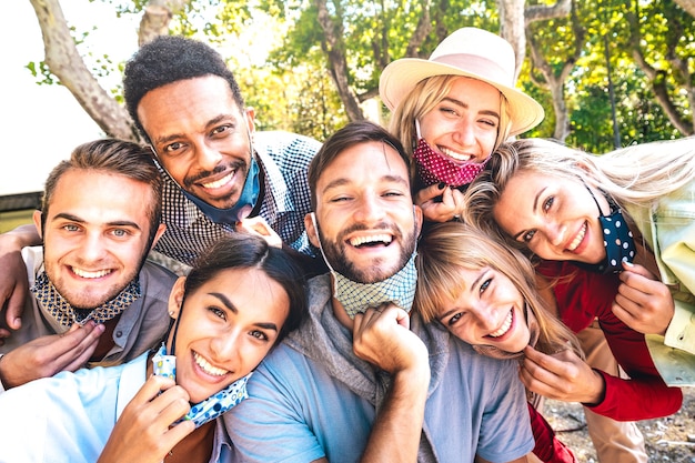 Amis multiraciaux prenant selfie heureux avec des masques ouverts après la réouverture du verrouillage