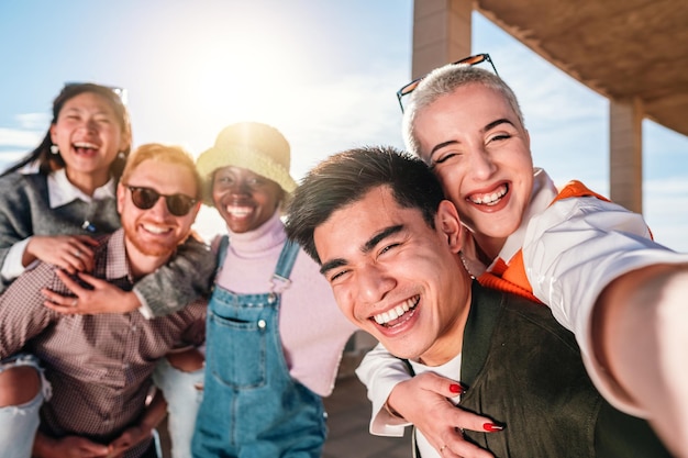 Amis multiraciaux prenant selfie heureux souriant à la caméra en journée ensoleillée