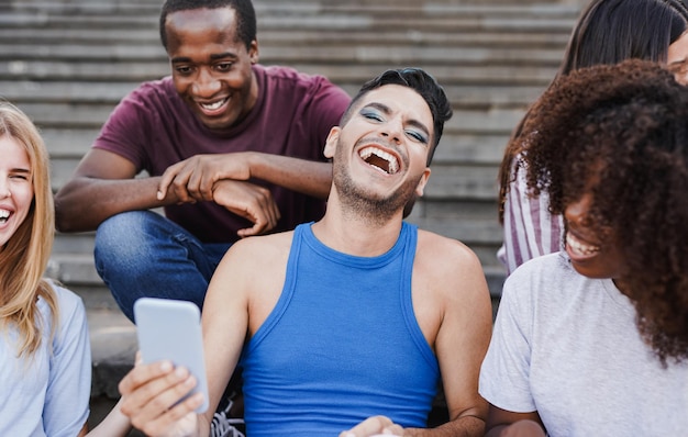 Amis multiraciaux utilisant un téléphone portable dans la ville Divers jeunes s'amusant en plein air