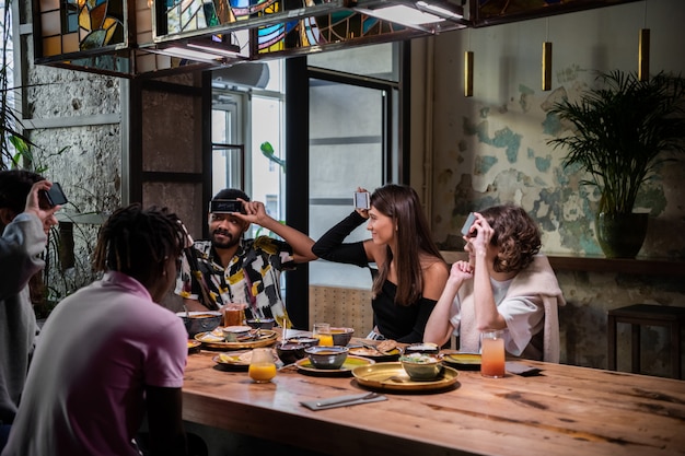 Amis positifs avec leurs smartphones sur le front assis à la table du dîner et essayant de deviner un mot écrit sur leur écran