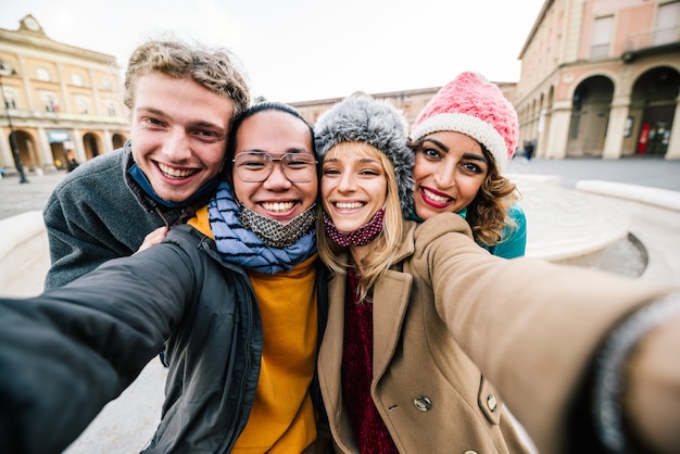 Amis prenant un selfie à l'extérieur de la ville - Nouveau concept de mode de vie normal avec des jeunes s'amusant ensemble en vacances avec un masque facial.