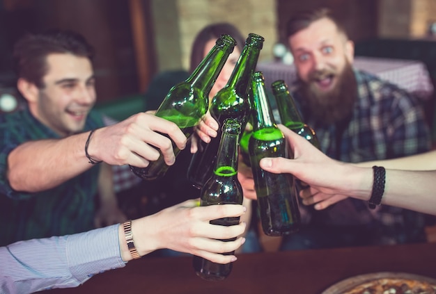 Amis prenant un verre dans un bar, ils sont assis à une table en bois avec des bières et des pizzas.