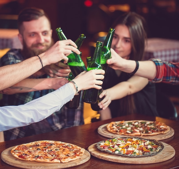 Amis prenant un verre dans un bar, ils sont assis à une table en bois avec des bières et des pizzas.