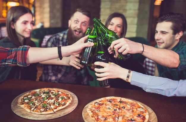 Amis prenant un verre dans un bar, ils sont assis à une table en bois avec des bières et des pizzas.