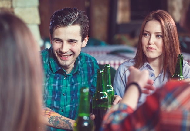 Amis prenant un verre dans un bar, ils sont assis à une table en bois avec des bières et des pizzas.