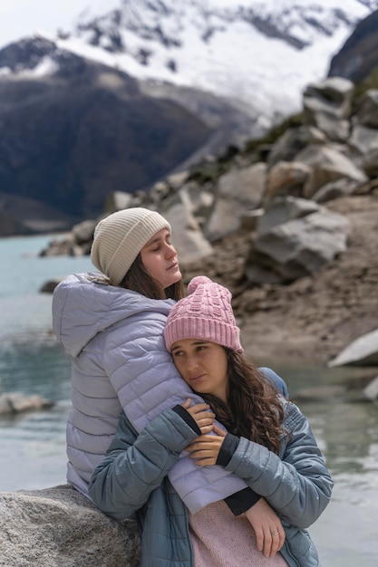 Amis s'embrassant au bord d'un lac avec des pics enneigés en arrière-plan