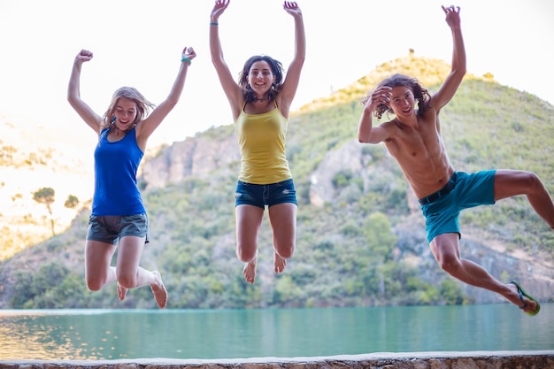 Amis sautant sur un talus sur un lac turquoise dans les montagnes