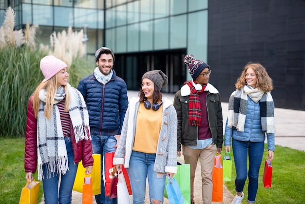 Amis se promenant dans la ville pendant la période de vente groupe multiracial de jeunes heureux et souriants après avoir acheté des cadeaux filtre de couleur vive