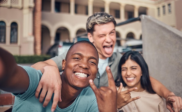 Amis selfie sourire et portrait sur le campus universitaire avec diversité visage heureux et drôle geste de la main et signe de rock Portrait heureux et étudiants de l'amitié interraciale et photographie