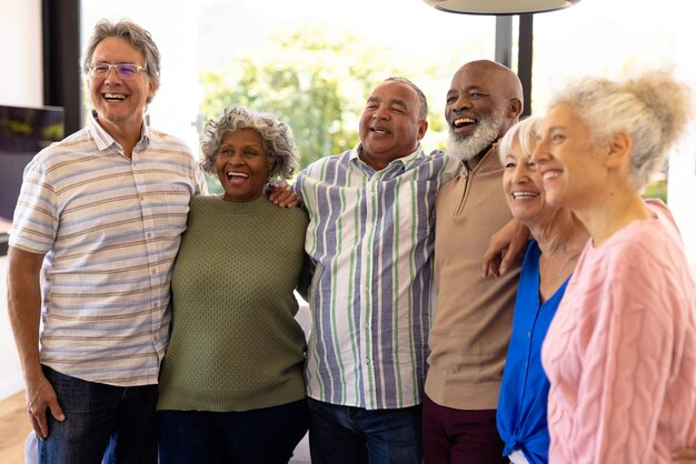 Photo des amis seniors multiraciaux avec les bras autour de rire et de détourner les yeux tout en se tenant dans une maison de retraite. joyeux, inchangé, amitié, convivialité, soutien, vie assistée et concept de retraite.