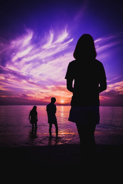 Des amis en silhouette debout sur la plage contre le ciel au coucher du soleil