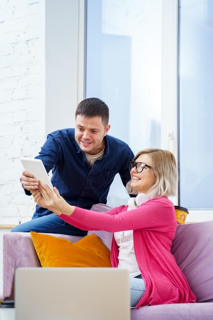 Des amis sont assis sur le canapé en train de discuter et d'utiliser une tablette