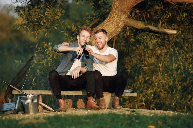 Des amis sont assis près d'un arbre et pêchent. Deux pêcheurs discutant et buvant une bière