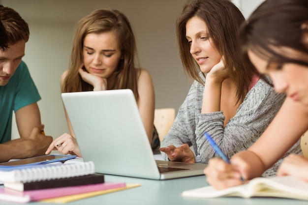 Amis souriants assis étudier et utiliser un ordinateur portable