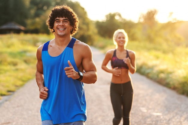 Amis souriants en bonne santé qui courent dans la nature. Homme aux cheveux bouclés au premier plan.