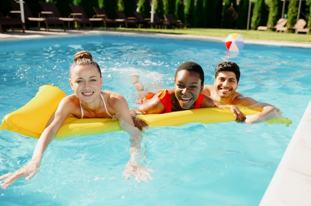 Des amis souriants nagent sur un matelas dans la piscine