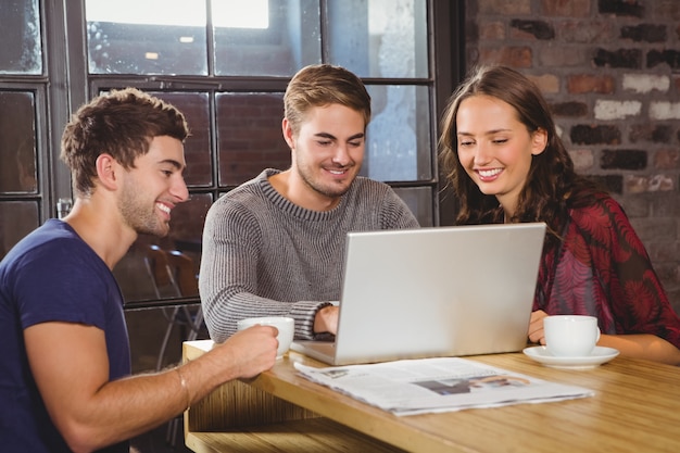 Amis souriants prenant un café ensemble et regardant un ordinateur portable