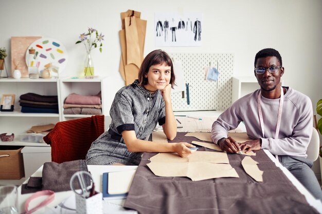 Amis souriants travaillant dans un atelier et créant des vêtements pour