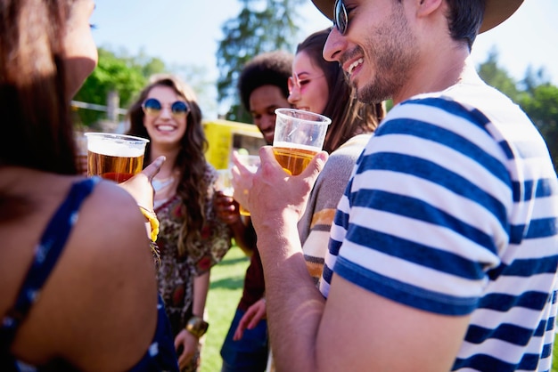 Des amis tenant de la bière dans des verres alors qu'ils se tiennent sur l'herbe.