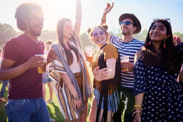 Des amis tenant de la bière dans des verres alors qu'ils se tiennent sur l'herbe.