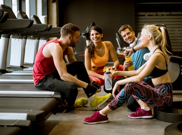 Amis en tenue de sport discutant et riant ensemble assis sur le sol d&#39;un gymnase après une séance d&#39;entraînement