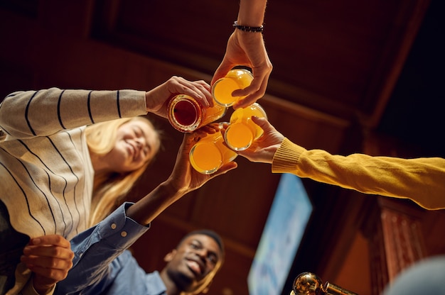 Les amis trinquent avec de la bière au comptoir du bar. Groupe de personnes se détendre dans un pub, mode de vie nocturne, amitié, célébration de l'événement