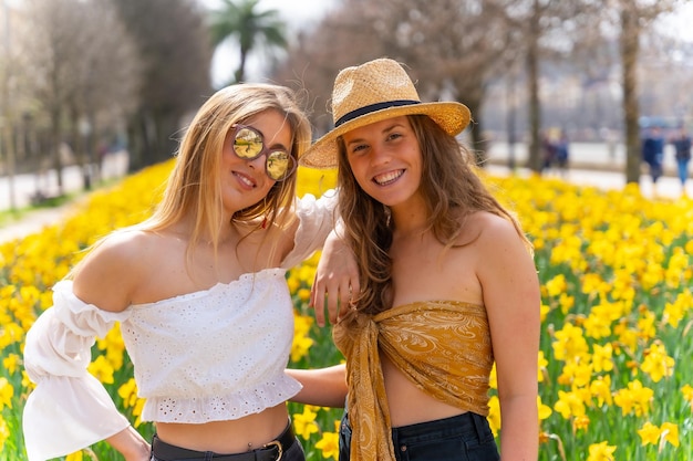 Amis en vacances dans la ville avec des chapeaux de paille à côté de belles fleurs jaunes souriant beaucoup et profitant du printemps