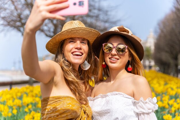 Amis en vacances dans la ville à côté de belles fleurs jaunes prenant un selfie avec le téléphone