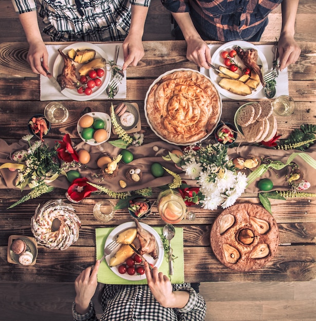 Amis de vacances ou famille à la table des fêtes avec viande de lapin, légumes, tartes, œufs, vue de dessus.