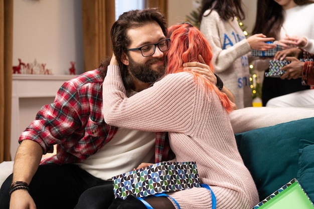 Amis de la veille de Noël assis sur le canapé un gars avec barbe et lunettes tient un cadeau