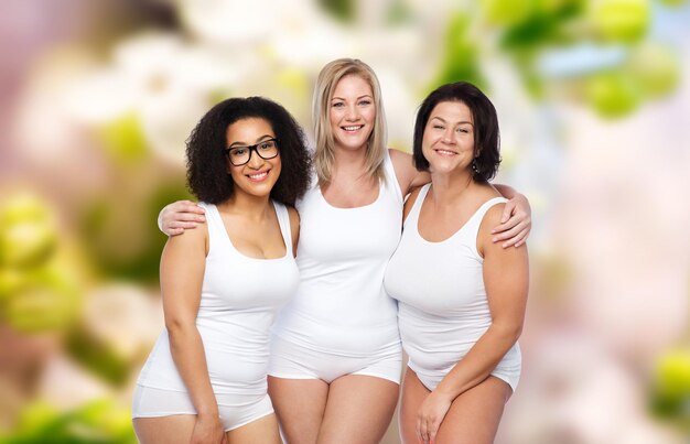 Amitié, beauté, corps positif et concept de personnes - groupe de femmes heureuses de taille plus en sous-vêtements blancs sur fond de printemps naturel