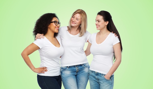 amitié, diversité, corps positif, concept de communication et de personnes - groupe de femmes heureuses de différentes tailles en t-shirts blancs étreignant et parlant sur fond naturel vert