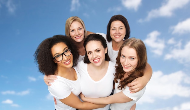 Amitié, diversité, corps positif et concept de personnes - groupe de femmes heureuses de différentes tailles en t-shirts blancs sur fond bleu ciel et nuages