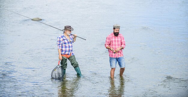 Amitié masculine Les hommes se tiennent dans l'eau La pêche est bien plus que du poisson Heureux pêcheur avec une canne à pêche et un filet Passe-temps et activité sportive Père et fils pêchant Week-end d'été Pêcher ensemble